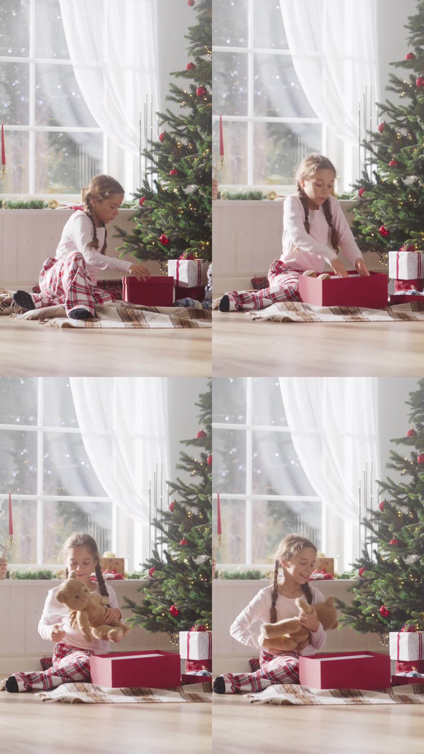 垂直屏幕:快乐的小女孩在节日早晨醒来，从圣诞树下收到新玩具。可爱的孩子迫不及待地从圣诞老人那里拿礼物