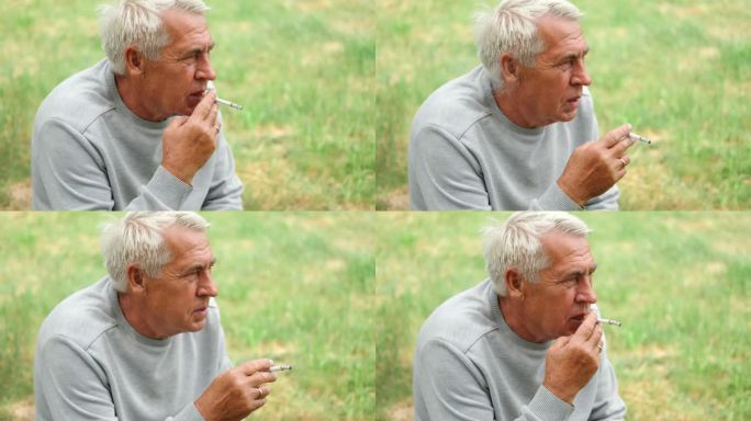 一位老人在户外点燃一支香烟，背景是绿色的大自然。沉思的老人一边抽烟，一边看向一边。特写脸。放松的退休