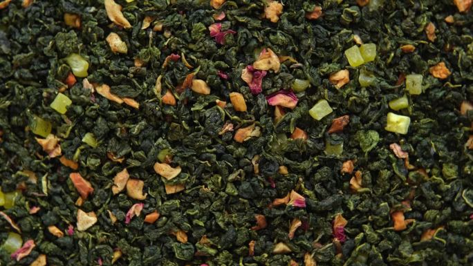 散叶芒果菠萝水果茶壁纸。混合红茶和绿茶干茶叶。特写，微距。前视图。纹理。干茶在旋转。摘要食品和饮料的