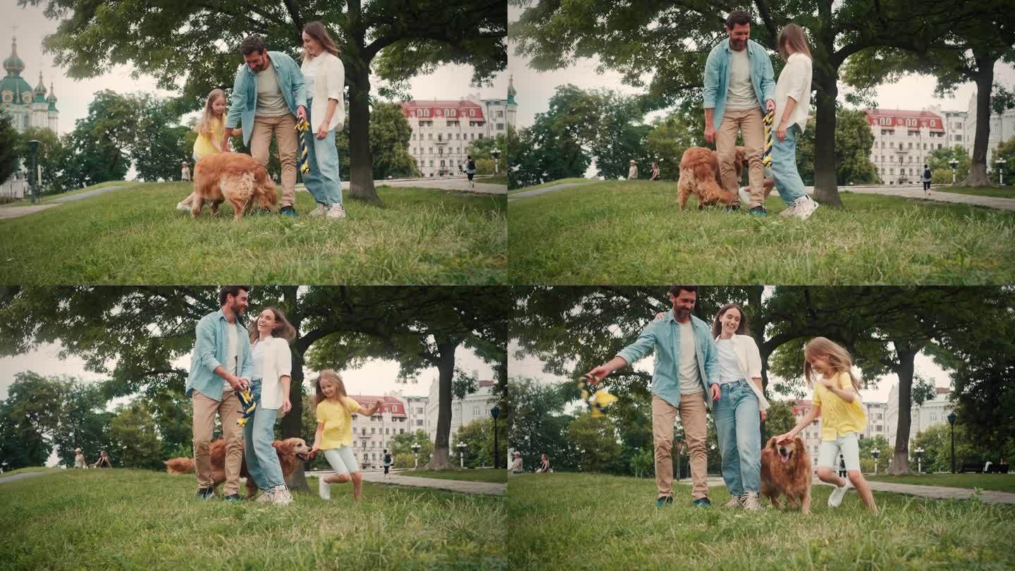 父母站在草地上，女儿抱着狗跑