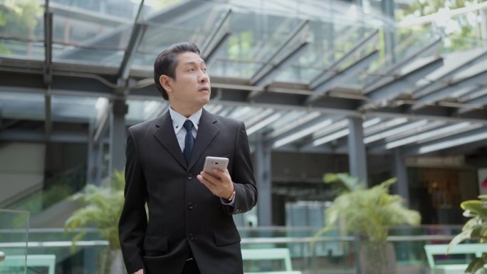 一位资深企业家走在一栋现代化的商业大楼里，一边用他的智能手机了解最新情况。