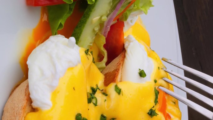 垂直视频吃素食荷包蛋，沙拉。美食家用叉子刺穿荷包蛋和面包上的蛋黄特写。吃素荷包蛋是健康的素食概念