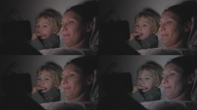 妈妈和儿子关着灯躺在床上，在黑暗的房间里用手机看卡通片