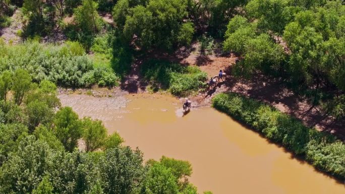 牛仔探险队骑在马背上穿过泥泞的河流，涉水穿越未知的领域，空中轨道