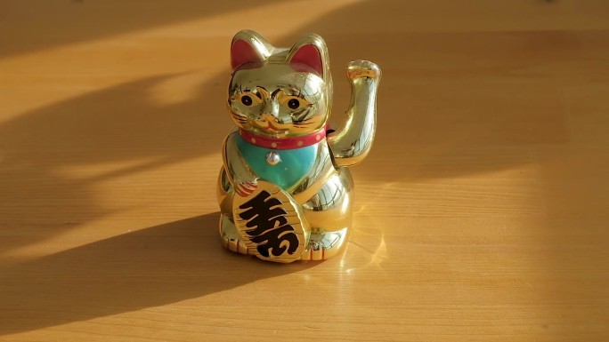 金色的幸运猫马尼基-尼科挥舞着爪子。木桌，灰色背景