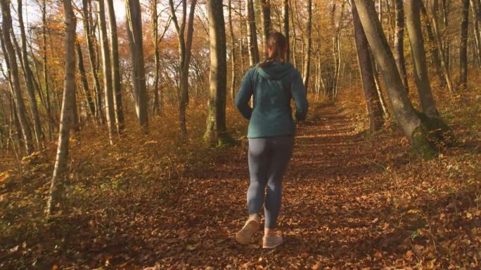 慢镜头:爱运动的女人和她顽皮的狗一起跑过秋天的森林