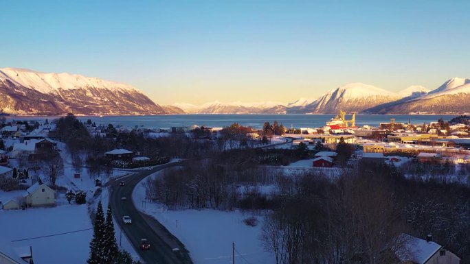 鸟瞰挪威峡湾风景小镇的冬季日落，汽车行驶在道路上