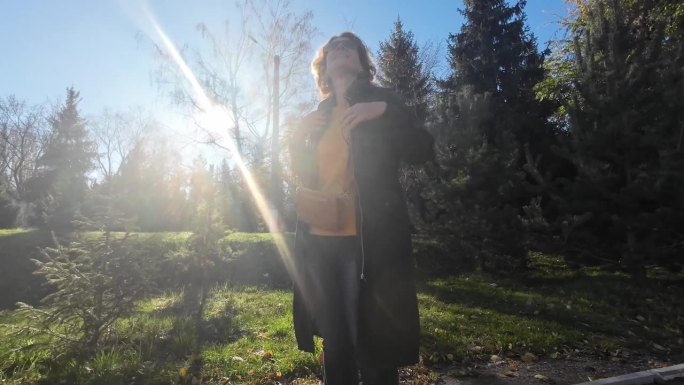 一个快乐的45岁女人站在阳光明媚的秋天的自然公园里，听着音乐，轻轻地跳着舞