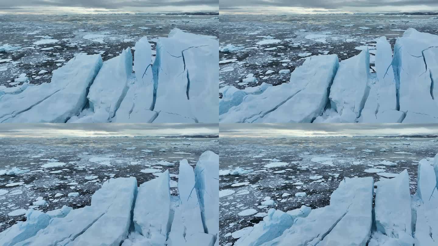 在格陵兰岛伊卢利萨特附近的巨大分裂冰山附近飞行。海洋中被雪覆盖的巨大冰山。空中北极自然景观，全球变暖