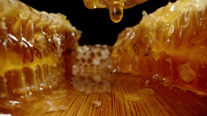 蜂蜜从蜂巢里滴到木桌上，从勺子上掉下来，相机从下面经过。多莉滑块极端特写。