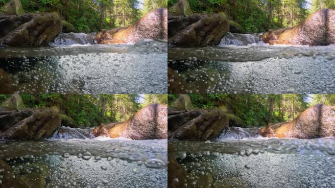 半水下的慢动作拍摄的溪流之间的石头与小瀑布。热带雨林中有一条清澈的河流。纯净的水和泡泡在丛林河