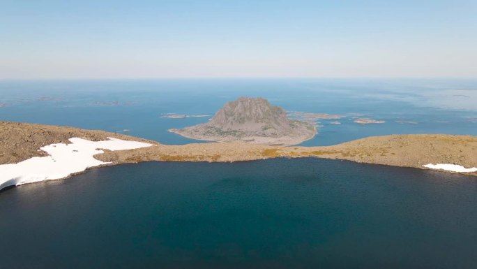 从挪威维加岛的最高峰俯瞰。这是一个有积雪的山湖，背景是矗立的石山Søla