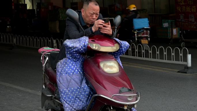 路口骑电动车的老年人使用智能手机