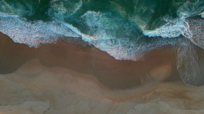 日落时分，沙滩上的浪花泛起白色泡沫。空中俯瞰海景或海洋沙滩