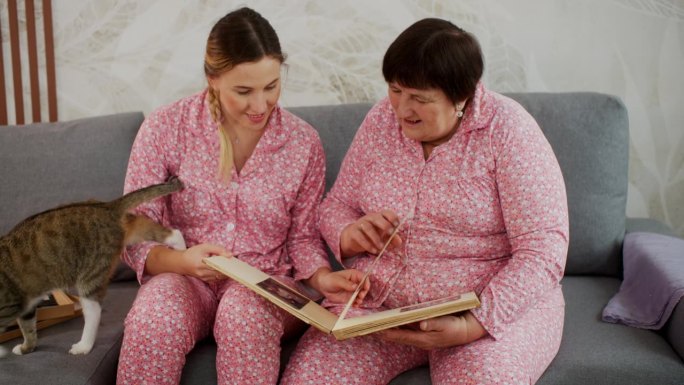 奶奶和穿着粉色睡衣的成年孙女带着猫在看家庭相册。