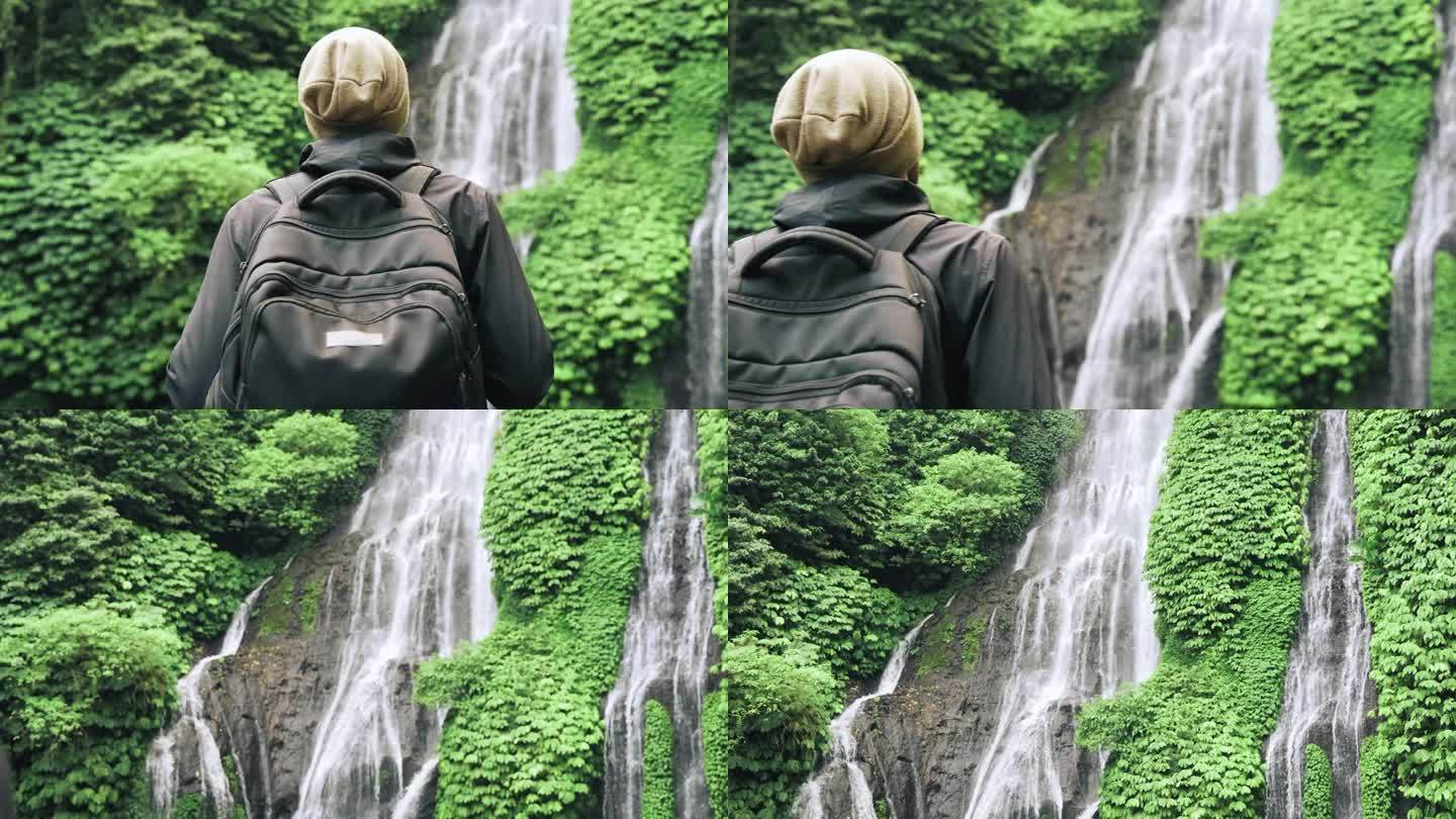 成年男子在绿色自然中前往森林瀑布。年轻人走到丛林瀑布旅行目的地的生活方式。天堂景观中的海岛之旅概念