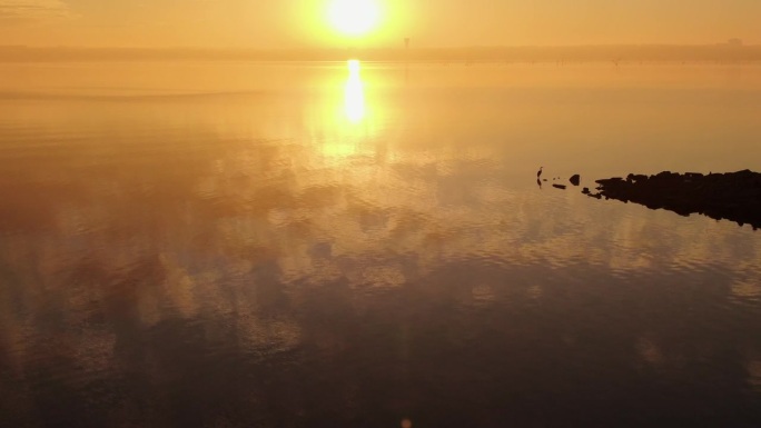 黄金时刻的光线穿过平静的湖面上的薄雾，在水面上反射出橙色的光芒