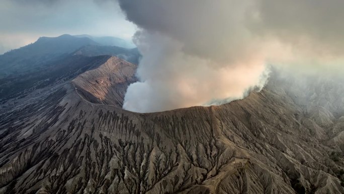 空中无人机拍摄的火山喷发日落场景，被云、雾和烟包围的Bromo火山与塞默鲁山、Batok和Widod