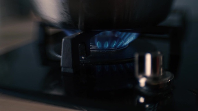 一个黑色陶瓷燃气灶滚刀被打开或点燃的扭曲镜头，火焰出现，一个铝锅放在炉子上。过了一会儿，把锅移开，关