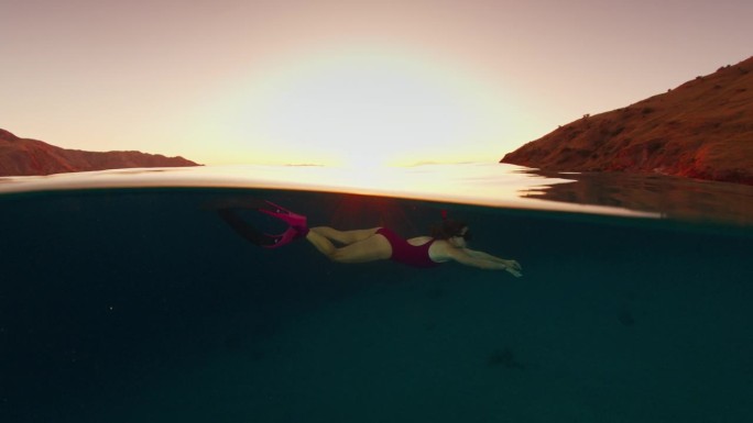 一名身穿粉色潜水服的女子在日落时分畅游在印度尼西亚科莫多国家公园的水下世界