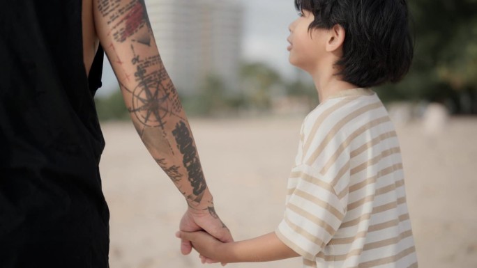 亚洲度假家庭的后景，慈祥的父亲牵着儿子的手沿着海滩散步。