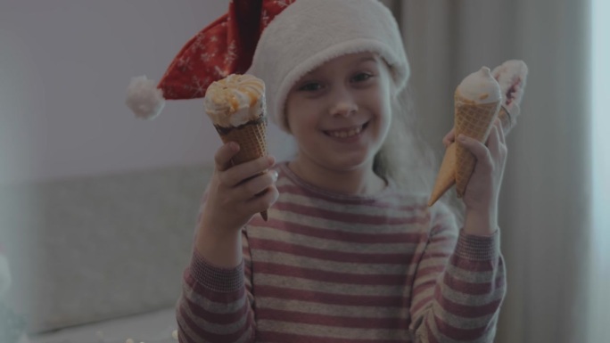 可爱的小女孩戴着圣诞老人的帽子，在圣诞晚会上吃了很多冰淇淋甜筒。变形镜头光晕。