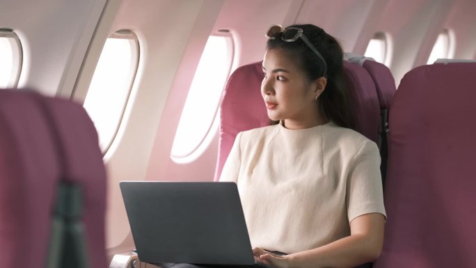 旅游和科技。坐头等舱。年轻漂亮的女商人坐在飞机上用笔记本电脑工作