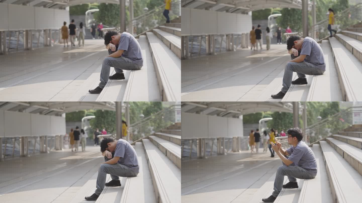 侧视图:一个亚洲人不舒服地坐在车站上，低着头，双手交叉，祈祷奇迹发生在他身上。