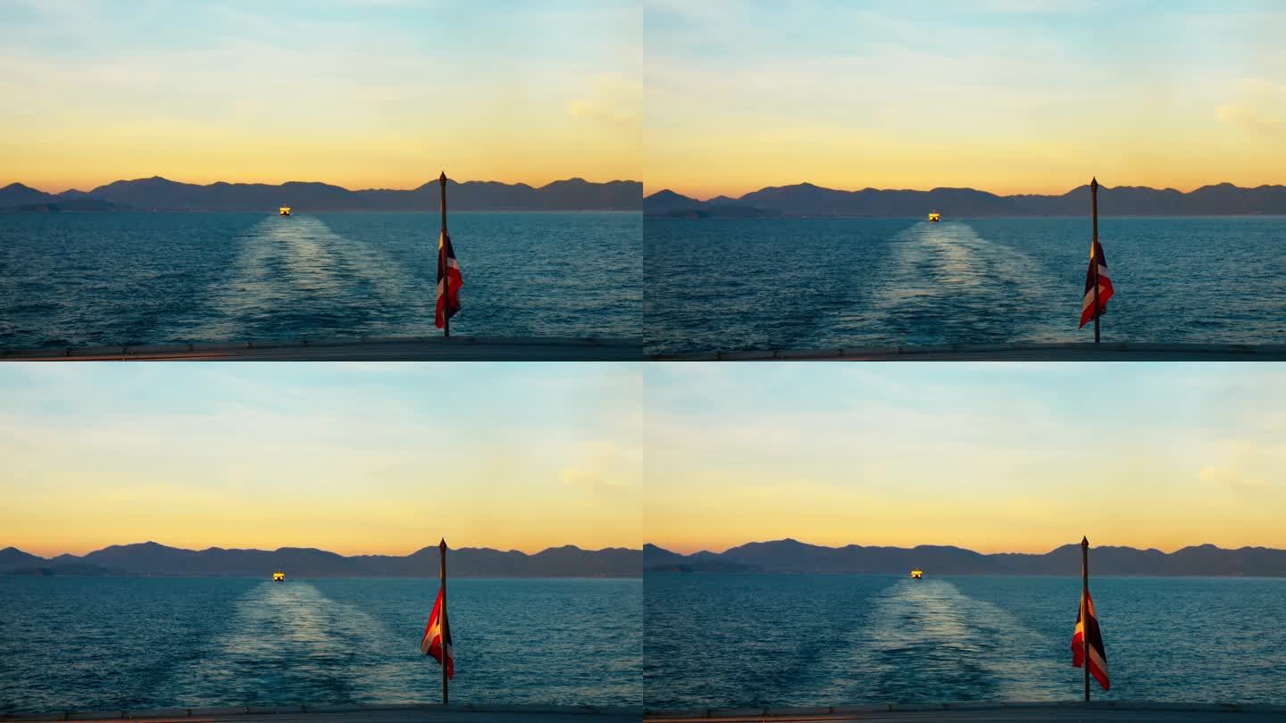 从船上看日落的美丽海景，慢动作。船旗在风中飘动的广角镜头，船在背景中航行。概念，在迷人的日落，船上平