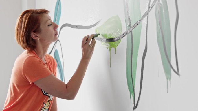 墙上的鲸鱼。成熟的短发女艺术家在墙上添加彩色鲸鱼。带有轻微平移镜头运动的镜头