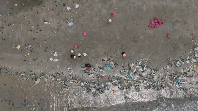 从空中俯瞰，戴竹帽的东南亚村民清理海滩上的塑料垃圾