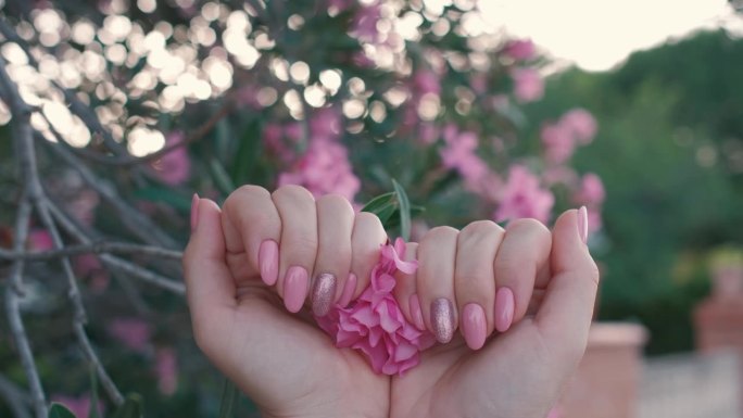 在一段4K慢动作视频中，女性的双手修剪整齐，指甲上点缀着粉红色的花朵。