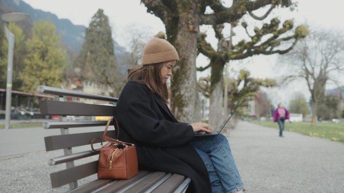 亚洲现代年轻女性在城市放松的同时在公园查看电子邮件。