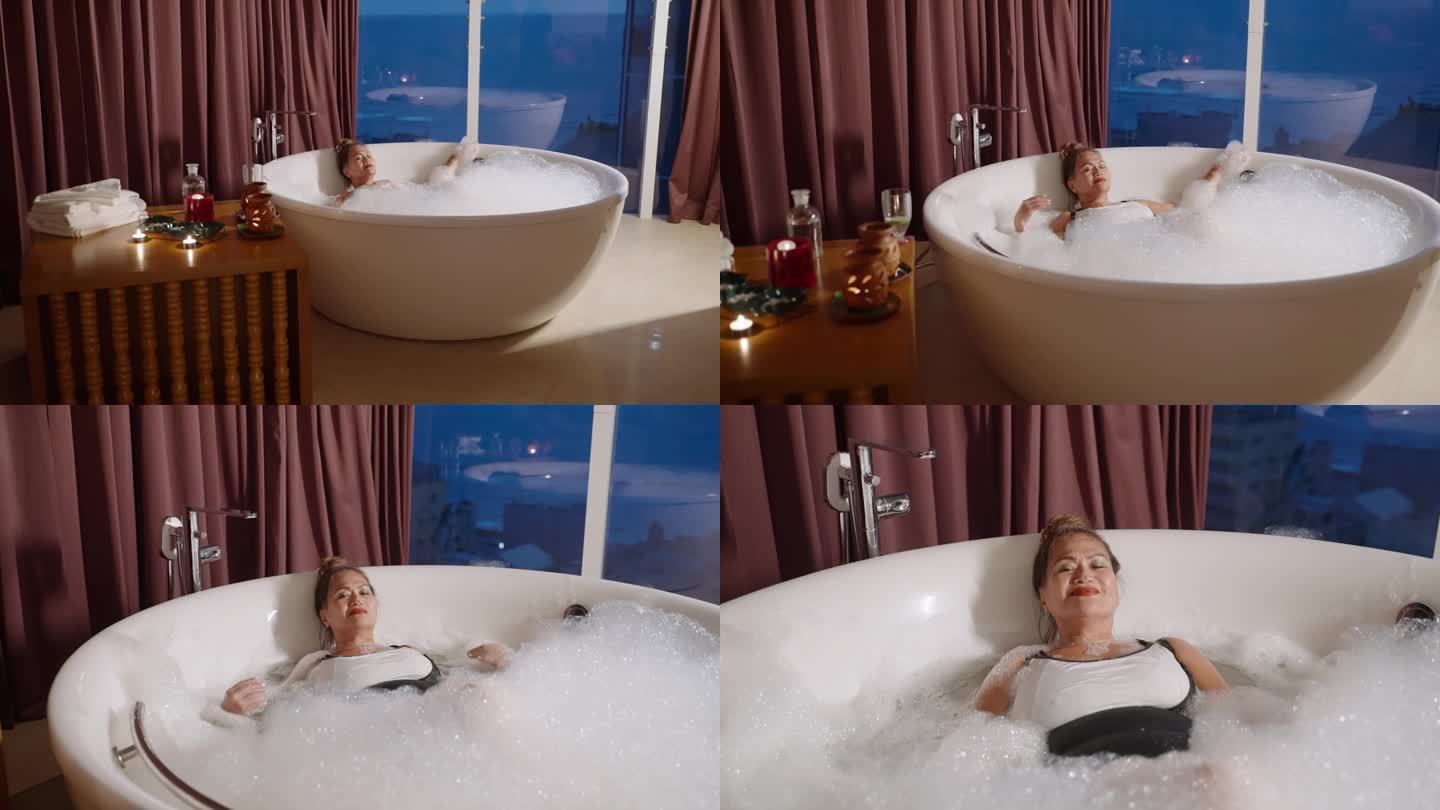 亚洲老年妇女在温暖的泡泡浴中放松。老太太喜欢在独立浴缸充满肥皂泡沫。成熟的双族女性在豪华水疗酒店浴室