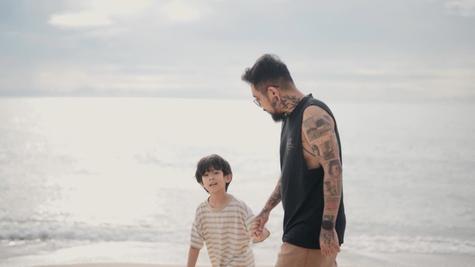 一个单身父亲牵着儿子的手走在沙滩上，他们一起度过了美好的家庭时光。