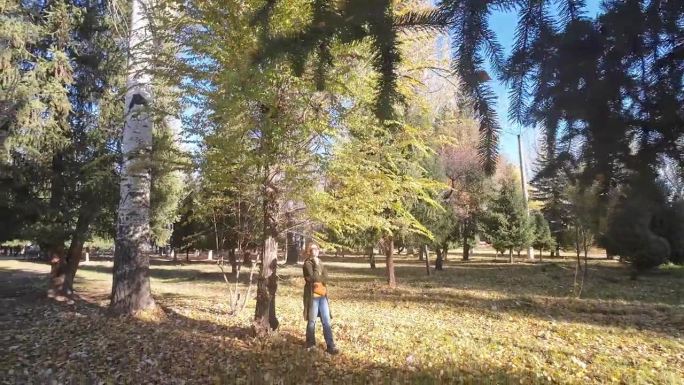 一个快乐的45岁女人站在阳光明媚的秋天的自然公园里，听着音乐，轻轻地跳着舞