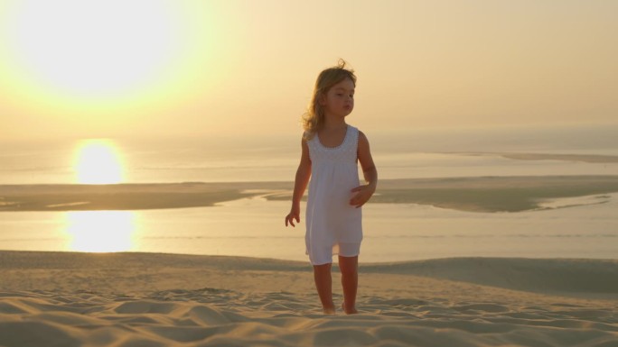 一个美丽的小女孩，穿着白色的裙子，赤脚走在沙滩上，夏日的黄昏，金色的夕阳映衬着大海，温暖的风吹皱了她