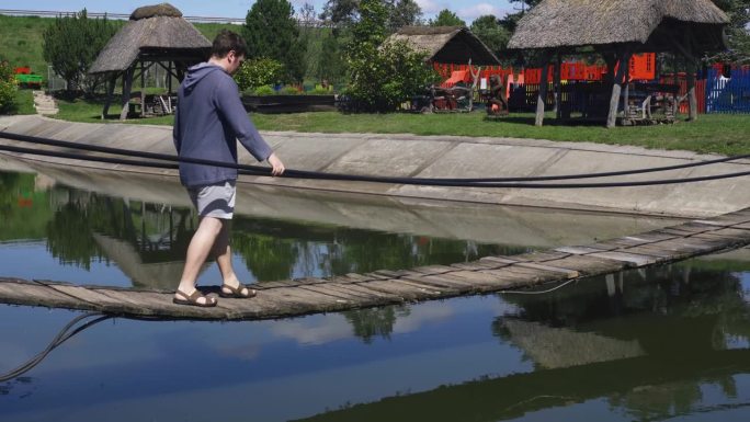 一个人走在池塘上的绳木桥上，保持着平衡。