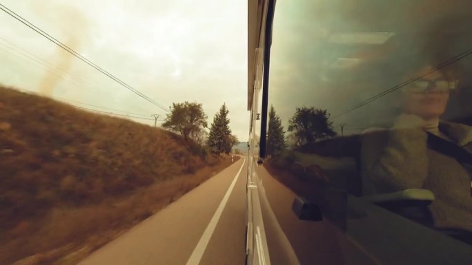 从窗外看，坐在露营车里的女乘客行驶在一条又长又直的路上，日落的黄金时间反射在玻璃上。旅游和交通。假期