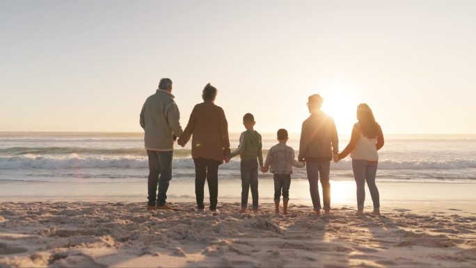 一家人手牵着手，背后的大海和阳光，祖父母和父母带着孩子在海滩上。爱，关怀和支持，假期和团结，女人和男
