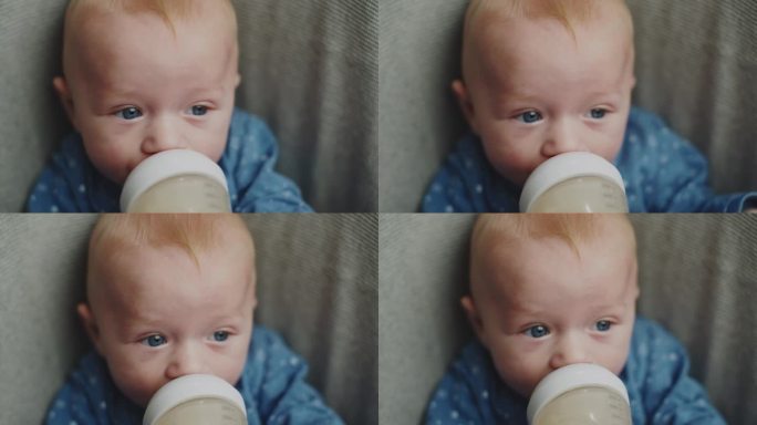 小男孩穿着蓝色的紧身衣坐在椅子上吮吸/喝着一瓶牛奶，小男孩吃东西的特写肖像，婴儿食品概念。饥饿的眼睛