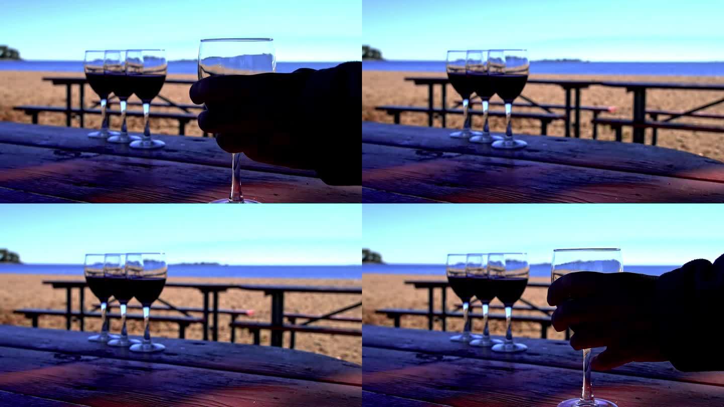 汉德从海滩外面的桌子上拿起盛酒的玻璃杯，慢镜头