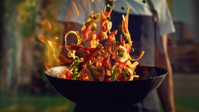 厨师在户外厨房用火锅炒菜。使用火焰技术烹饪食物的人，在平底锅中点燃热油和酒精。特写超级慢动作镜头