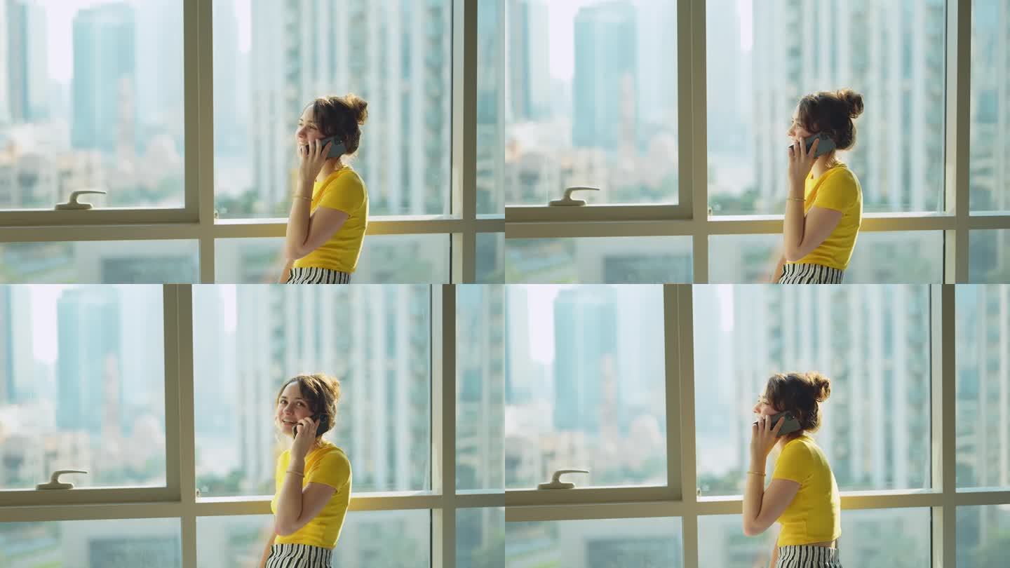 一个女人站在能看到市中心风景的窗口边打电话