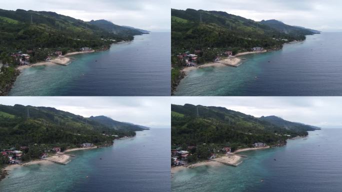 菲律宾沿海房屋沿着海岸线道路在热带郁郁葱葱的绿色杂草丛生的山麓宿务岛。空中摄影车