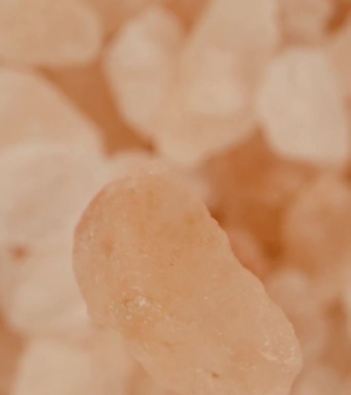 一粒粉红色的海盐落在一簇盐上，微距放大，俯视视图。垂直视频。
