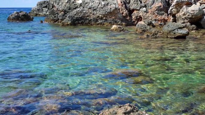 希腊科孚岛Limni海滩清澈的海水，海底有大而圆的石头，海岸背景上有锋利的岩石