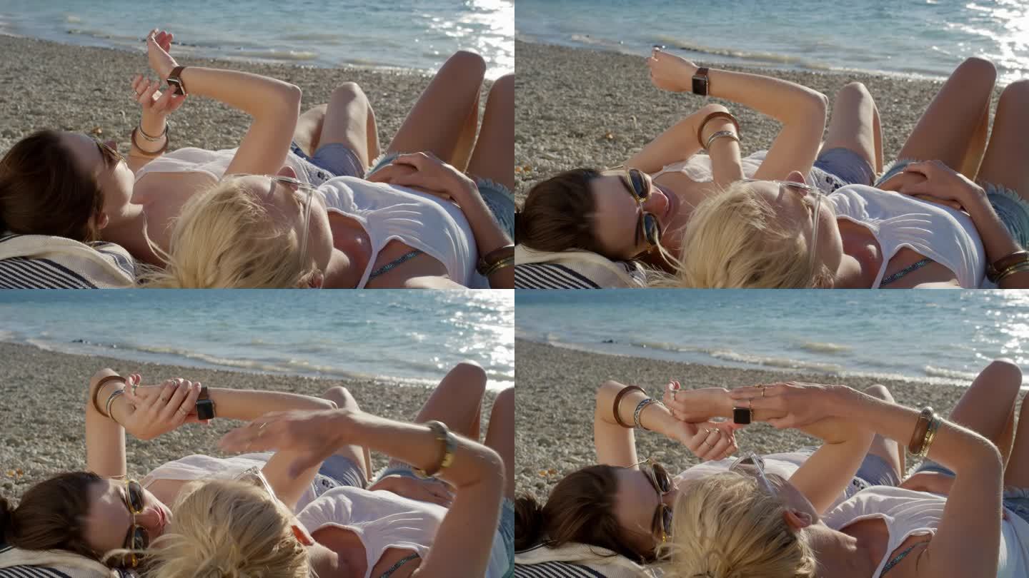 两个女人在海滩上放松，用智能手表发短信，看日落，最好的女朋友一起出去玩，温暖的自然光在清澈的水面上闪