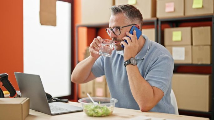 头发花白的男子在办公室用智能手机谈电商业务，喝着水