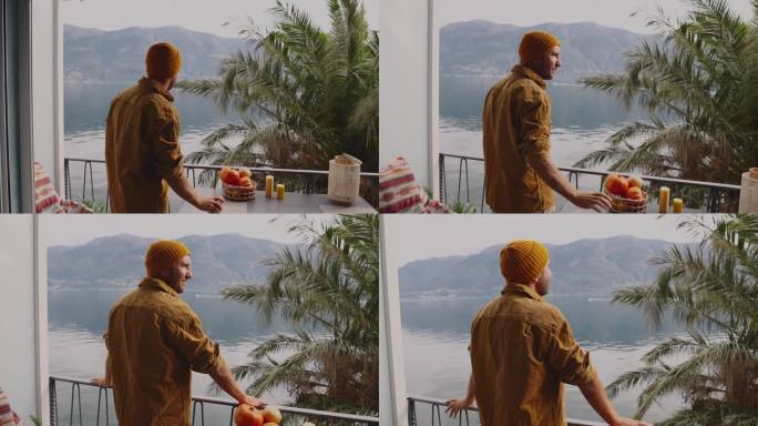 慢镜头:男子端着一杯茶走在阳台上，看着山景湖景